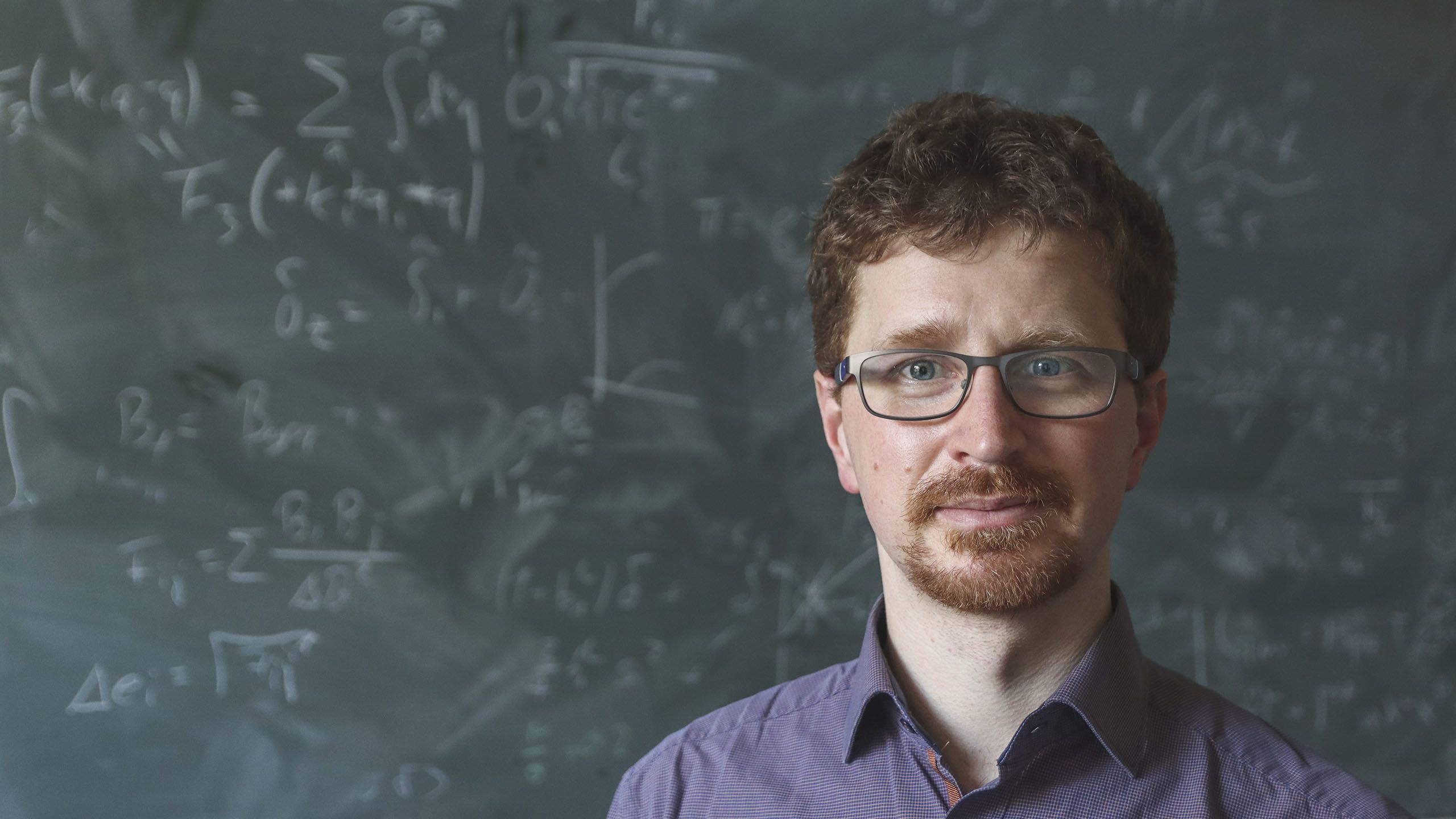 Dr Tobias Baldauf standing in front of a blackboard with equations written on it in chalk 