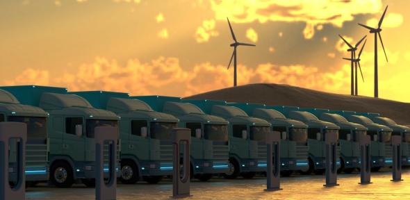 A row of clean energy trucks, wind turbines in the background