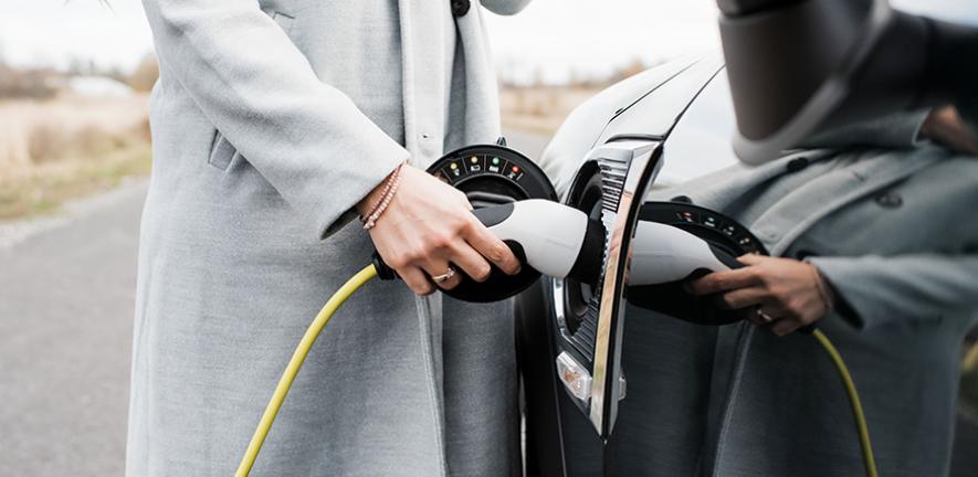 View of woman's hand plugging in charging lead to her electric car