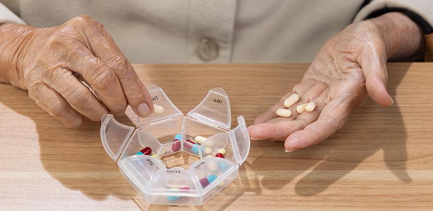 Elderly woman putting pills into pill box for the week - stock photo