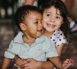 Photograph of a young girl hugging a baby boy