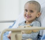 A little boy with a shaved head is smiling as he is laying on a hospital bed.