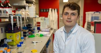 Cancer researcher Tom Else sitting in a lab wearing a white lab coat