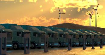 A row of clean energy trucks, wind turbines in the background