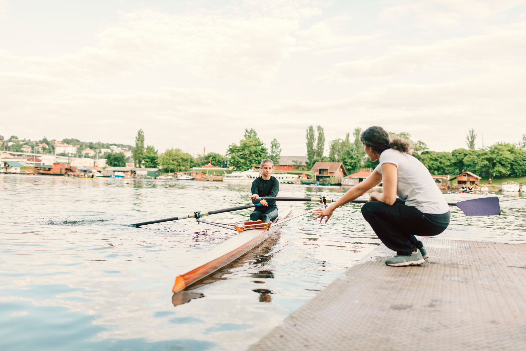 A girl in a rowing boat, coming in to the pontoon with a woman giving instruction from dry land