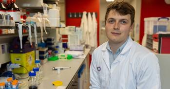 Cancer researcher Tom Else sitting in a lab wearing a white lab coat