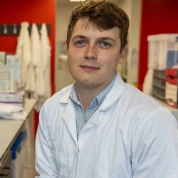 Cancer researcher Tom Else sitting in a lab wearing a white lab coat